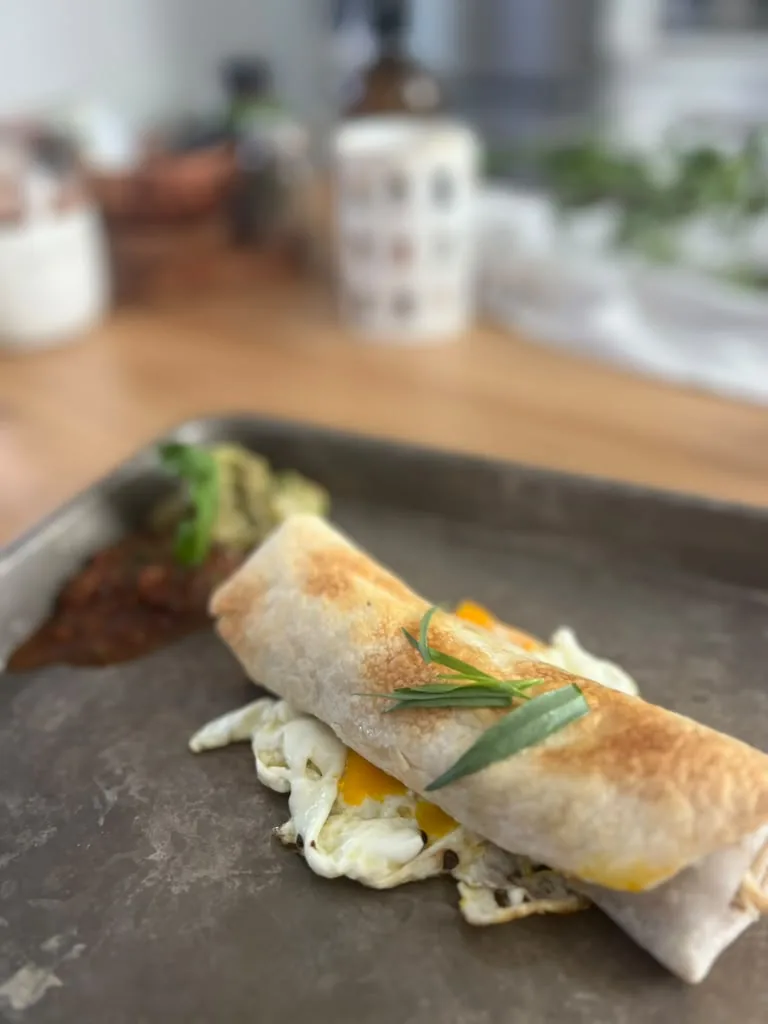 A breakfast wrap on a tray beside a fried egg, finished with rosemary