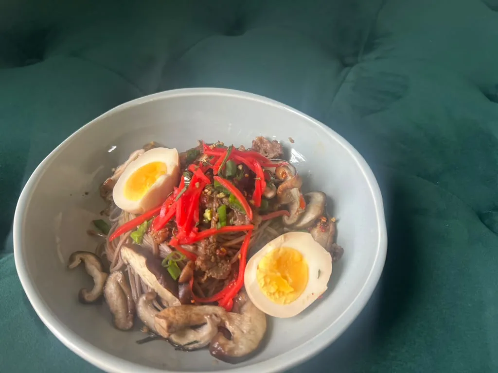 A noodle bowl with soft-boiled eggs, mushrooms and sliced red chilli