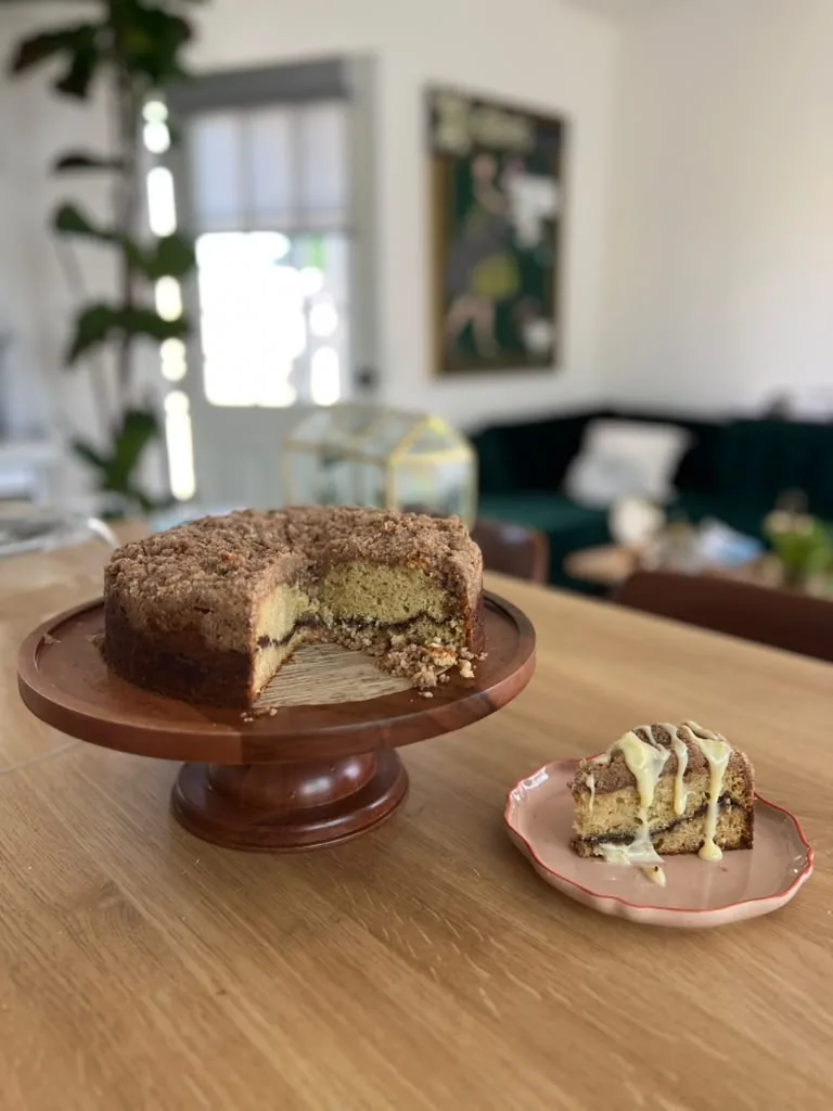 A cake on a wooden stand, cut open to show a green pistachio centre, one slice on a pink plate