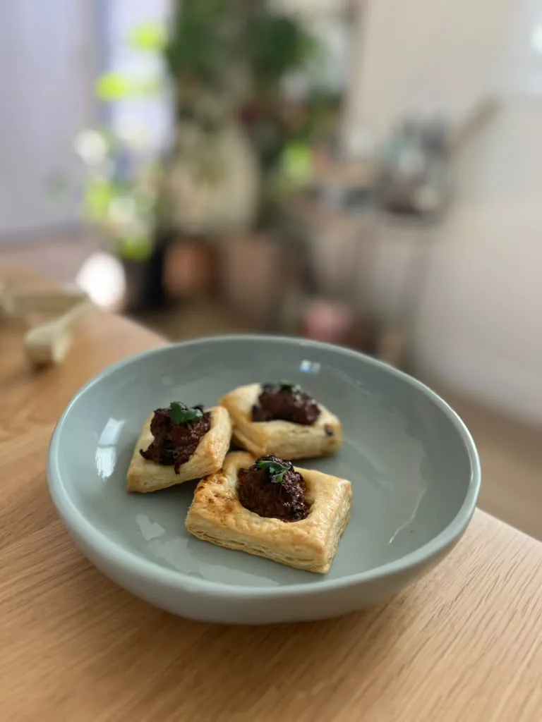 Puff pastry bites topped with a dark, glossy relish on a green plate