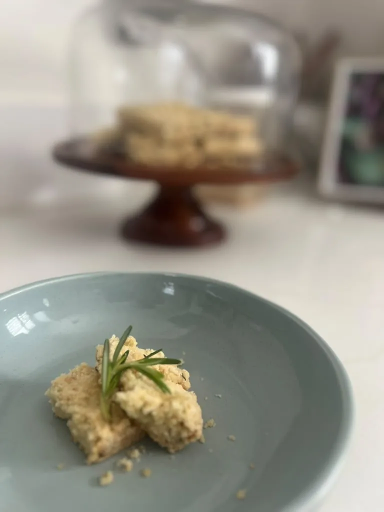 Two pieces of shortbread plated with rosemary, a cake stand behind
