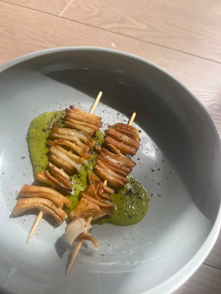 Scored, glazed skewers fanned across a pool of herb oil in a pale bowl
