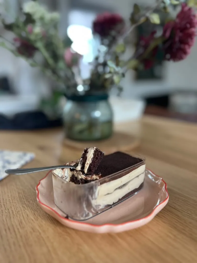 A slice of layered tiramisu with a dark cocoa top, on a pink scalloped plate